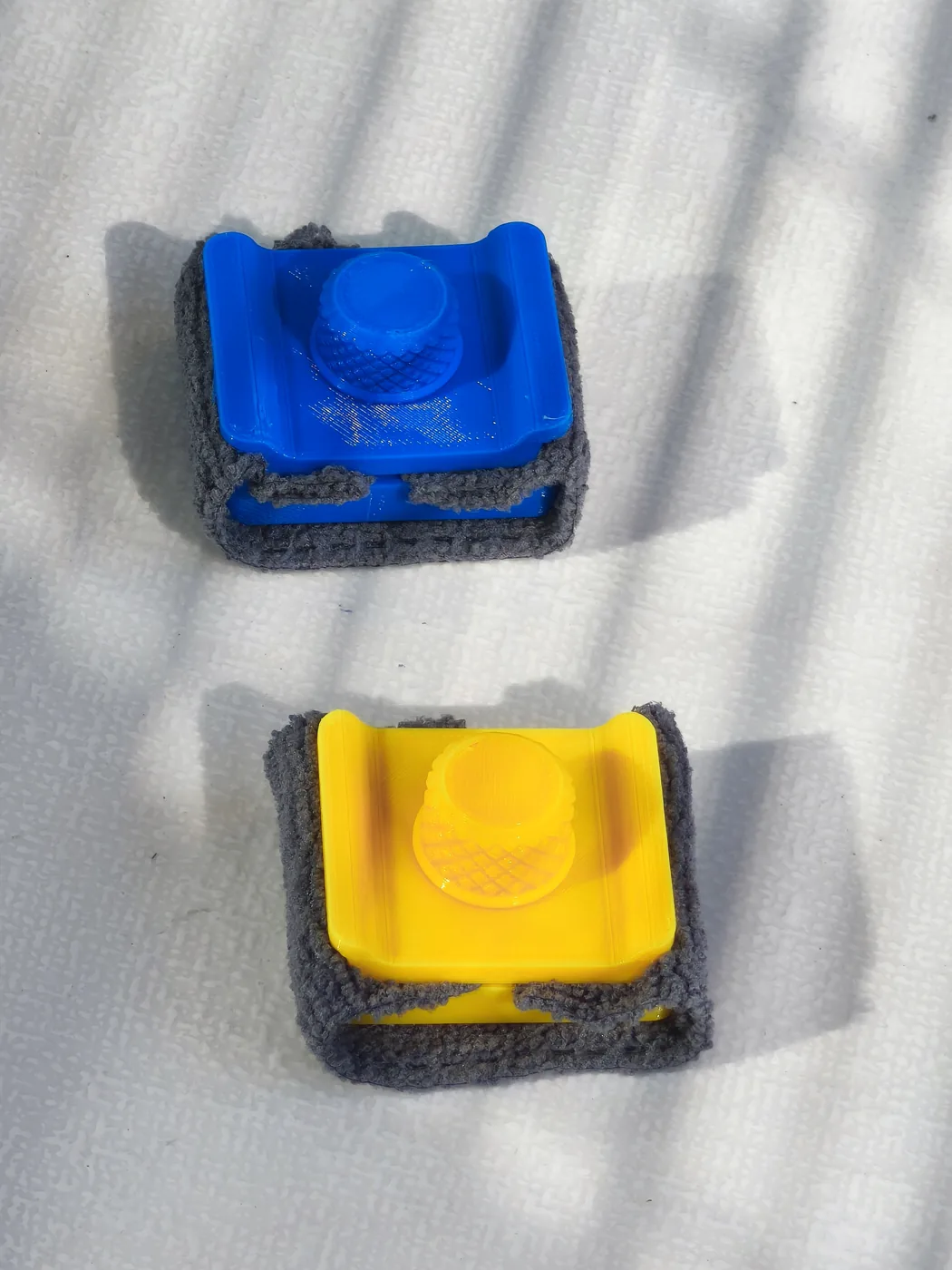 Vue de dessus de deux tampons de nettoyage imprimés, bleu et jaune, posés sur une surface blanche